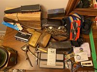 Overview of men's grooming items including vintage razors, brushes, combs, sunglasses, and accessories on table with lot tag.