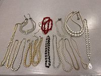 Full view of all 14 necklaces laid flat showing sizes, bead colors, and styles mostly faux pearl and glass beads.