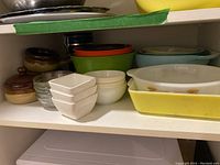 Shelf with multiple bowls and dishes including brownware onion soup crocks, clear glass small bowls, white square ceramic bowls, and colored plastic bowls