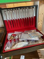 Photo of the flatware knives neatly arranged in the red felt-lined wooden box with additional items in the box below.
