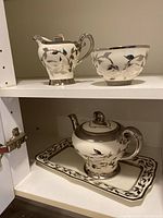 Shelf view showing creamer, sugar bowl on top shelf, teapot with lid and rectangular tray on bottom shelf