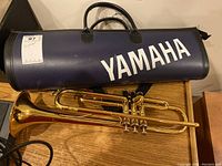 Yamaha trumpet laid out with cylindrical case on wooden surface