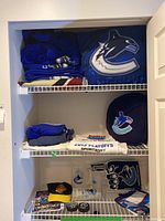 Shelf showing folded blue Vancouver Canucks clothing including an XL jersey, 2013 playoffs towels, and fan accessories like a drawstring bag and cap.