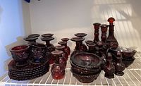 Full display of the lot showing ruby red glass stemware, decanter, candlesticks, bowls, salt and pepper shakers, and dishes all arranged on a shelf.