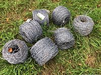 Seven rolls of barbed wire laid out on grass