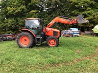 Left side view showing enclosed cab, front loader arms raised and bucket attached