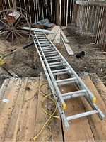 Full view of two aluminum ladder sections laid on wooden planks in barn with dirt and debris around.