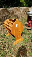 Side view of wooden saddle holder rack outdoors on grass with hay bales in background.