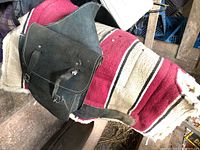 Close-up and full view of black leather saddle bag showing buckles, strap and stitching.