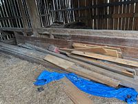 Wide view of assorted barn boards and lumber stacked against a barn wall