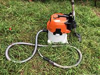 Stihl wet/dry vacuum unit with hose and floor attachment set on grass.