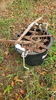 Lot of assorted horse tack and saddle parts arranged on a black round container outdoors with grass and leaves around.