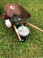 Rusty metal wheelbarrow on grass holding hydraulic fluids and garden sprayer