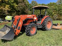Side profile of Kubota M7060DTH1 tractor with M21 front loader and conventional bucket parked on grass