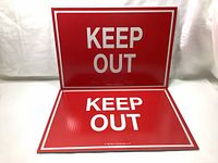 Two red KEEP OUT signs, one standing, one laying flat, on a white surface with a white backdrop.