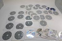 Array of 36 Apple software recovery and installation CDs laid flat, most in paper sleeves, on white background.