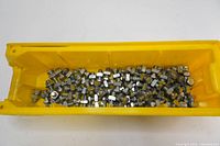 Yellow container filled with stainless steel bolts and nuts loosely piled inside.