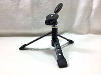 Mini black tripod with three foldable legs and rubber tips, placed on a flat surface.