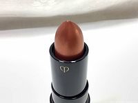 Close-up view of the lipstick showing the orange pearl shade and black tube with logo.