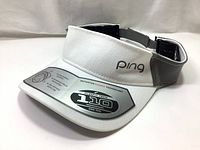 Front and side angled view of the white PING golf sun visor cap showing the FlexFit Tech 110 One Ten sticker and gray embroidered logo.