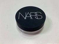 Photo of the top of the NARS loose powder container, showing black lid with white NARS logo.