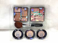 Top view of blush and bronzer powder compacts alongside three strobe powders and makeup brush in clear plastic tray.