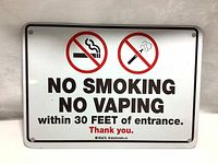 Full view of no smoking no vaping sign, showing entire metal rectangular panel with text and symbols. Slight wear marks.