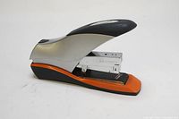 Side view of Swingline 70 sheet desktop stapler showing orange base, silver metal stapling mechanism, and black handle.