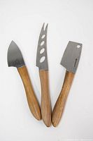 Three Swissmar cheese knives arranged side by side showing acacia wood handles and stainless steel blades of different shapes for various cheese cutting tasks.