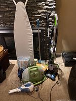 Photo showing all items including ironing board, Bissell Green Machine carpet cleaner, upright floor cleaner, handheld vacuum, mop, and boxes.