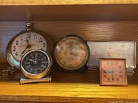 Photo of five assorted clocks on wooden shelf showing various styles and sizes.