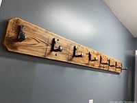 Full side view of the custom coat hanger mounted on wall showing eight metal hooks from railroad spikes attached to the wooden plank.