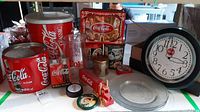 Overview of Coca-Cola themed items including large and small metal containers, glass pitcher, wall clock, glass dishes, and decorative tins.
