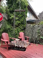 Photo of hanging fire pit suspended by chain on a backyard red deck with outdoor chairs in the background.