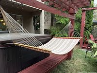 Full view of outdoor hammock hung between wooden posts with hot tub and patio in background.