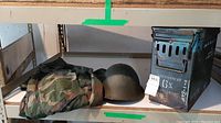 Shelf display showing all three items: helmet, camouflage flight suit, metal box