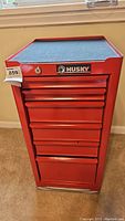 Front view of red Husky tool box with six drawers, lock in center, and blue mat on top