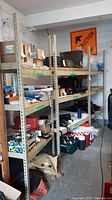 Two metal shelving units filled with various items including a cooler, boxes, and tools. One unit is 48x36x84 inches, the other 36x36x84. Shelving shows wear and damage.