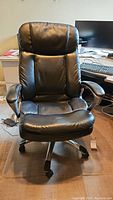 Front view of black leather office chair showing cushioned padded seat and backrest, and wheeled base.