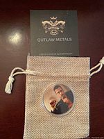 Certificate of authenticity and coin in a drawstring pouch with Outlaw Metals branding.