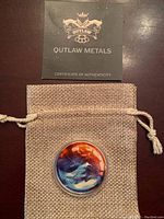 Top view of coin in capsule placed on grey drawstring pouch with certificate of authenticity card from Outlaw Metals above it.