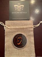 Photo of the coin in protective capsule on burlap pouch with Outlaw Metals certificate of authenticity above