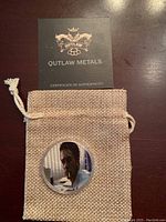 View of coin inside burlap pouch with Outlaw Metals certificate behind