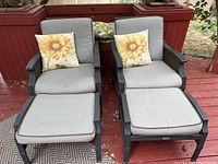 Front view of two patio chairs with light gray cushions and matching stools with sunflower-patterned pillows on chairs.