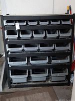 Front view of the black shelving unit with multiple grey plastic bins fitted on wire rack shelves.