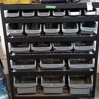 Front view of black metal shelving unit holding 20 grey plastic bins arranged in 5 rows of 4 bins each. Bins slot into wire shelves, one chip visible on bin front.
