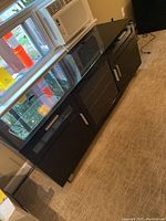 Full front view of black TV stand showing tinted glass cabinet doors and chrome hardware