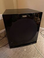 Front view of the black glossy Velodyne subwoofer with fabric speaker cover and visible vent slot at the bottom.