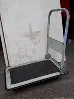 Full view of wheeled platform cart with handle upright showing metal frame and black rubber platform.