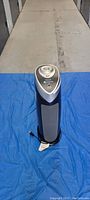 Full view of tower air purifier placed vertically on blue cloth, showing front vents and power cord.